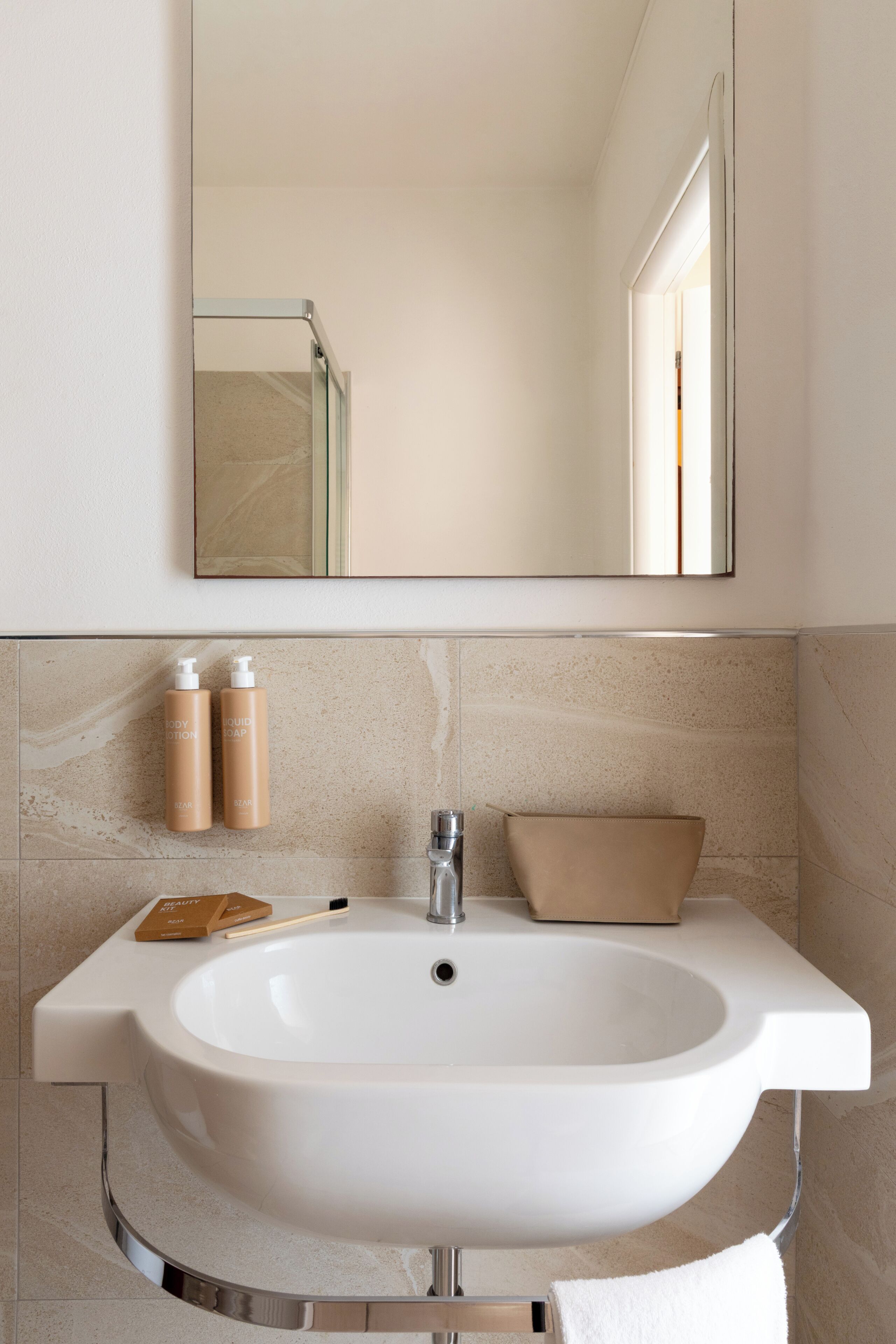 A bathroom with a large white sink, two bottles of body lotion, a toothbrush, and a towel.