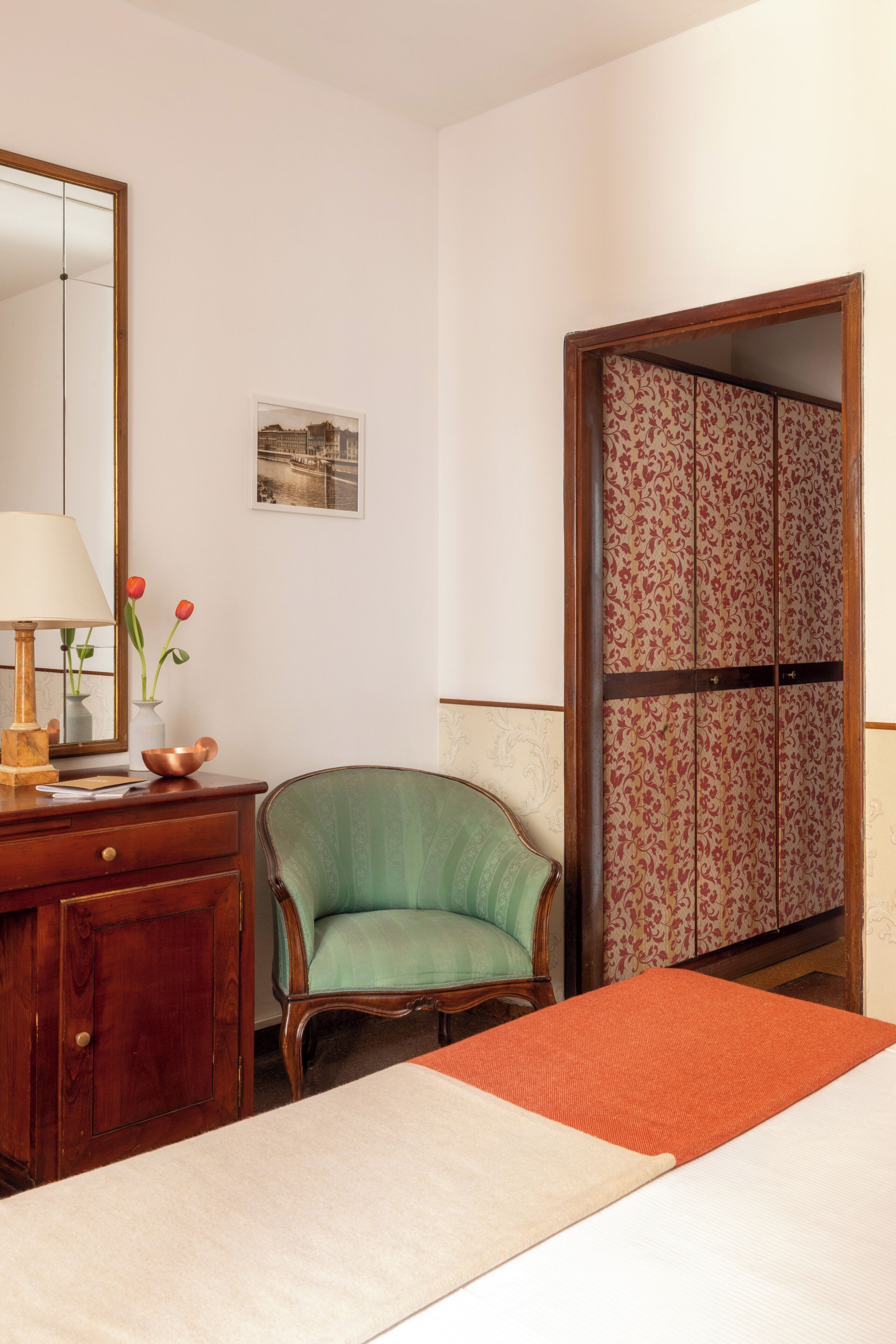 A room with a bed, a green armchair, a wooden dresser, a mirror, and a traditional sliding door.