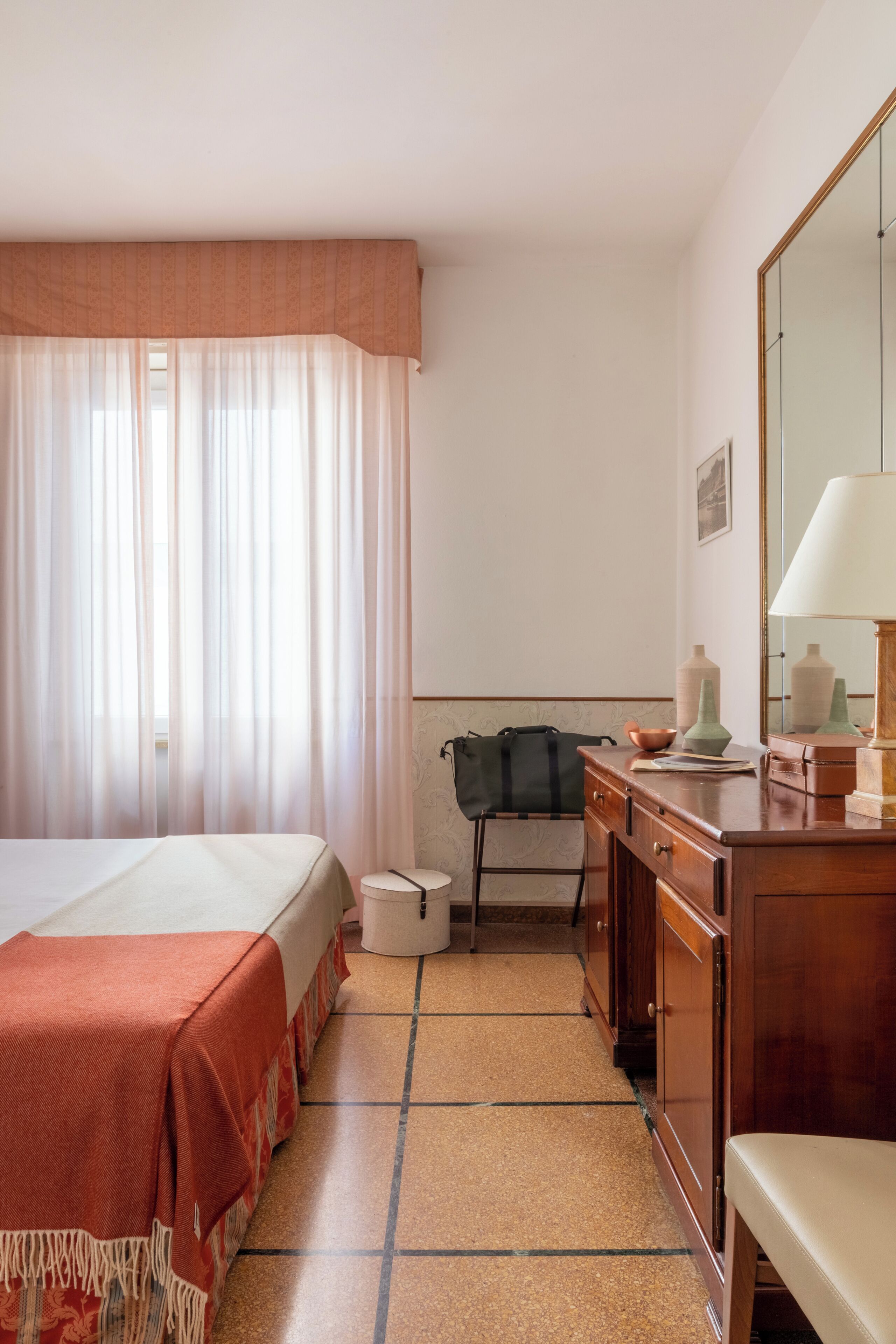 A hotel room with a bed, a desk, a chair, a lamp, and a mirror.