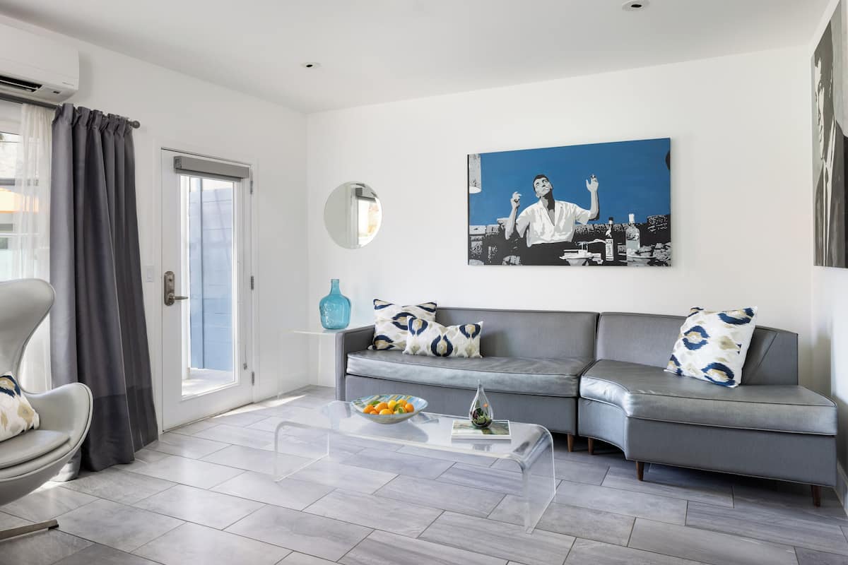 A modern living room with a grey sofa, a glass coffee table, and a painting on the wall.