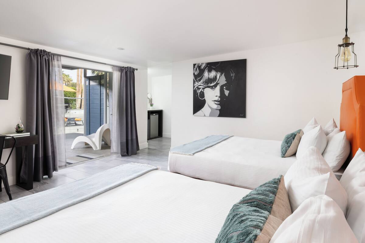 A modern hotel room with two beds, a desk, and a large window with curtains.