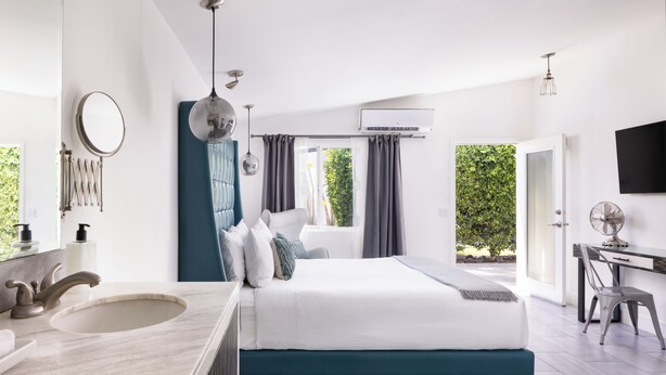 A modern bedroom with a large bed, a bathroom with a sink, and a desk area.