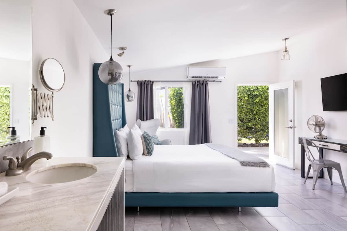 A modern bedroom with a large bed, a bathroom with a sink, and a desk area.