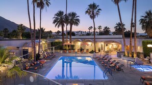 A pool area with lounge chairs and a fire pit, surrounded by palm trees and a mountain in the background.