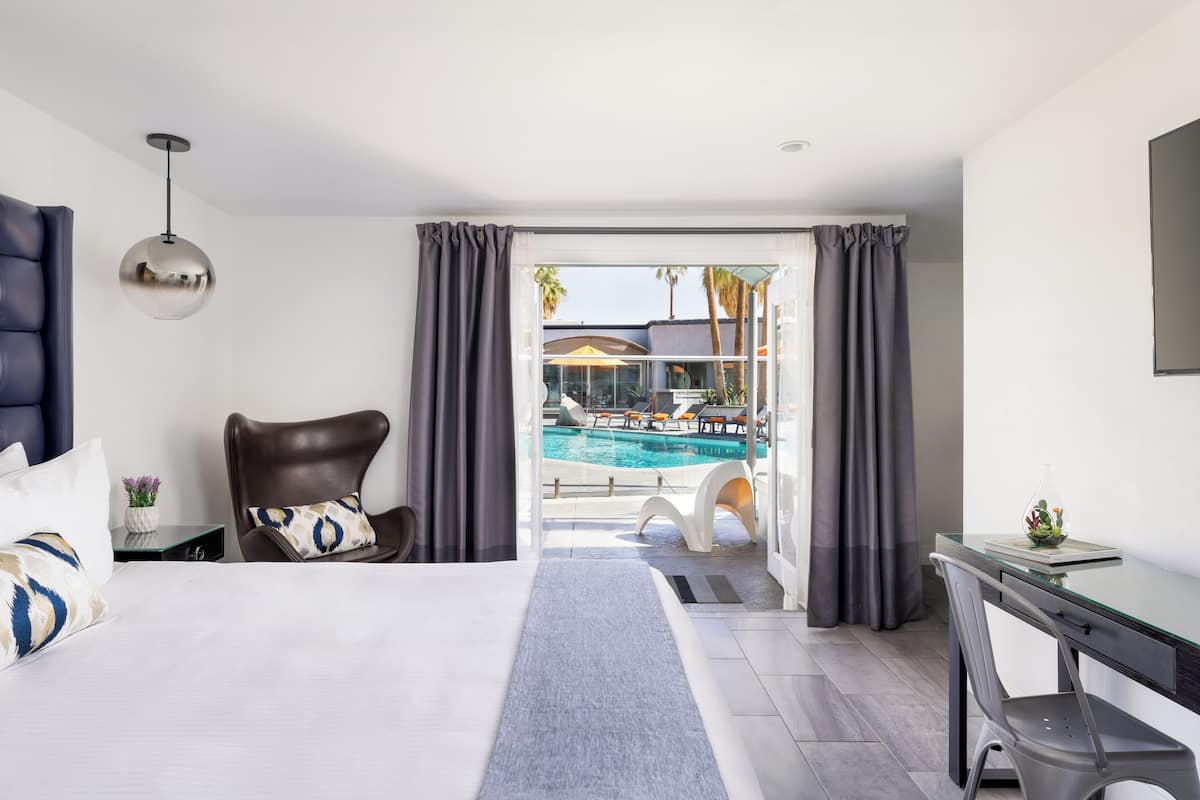 A hotel room with a bed, a desk, a chair, a view of a swimming pool, and a balcony.
