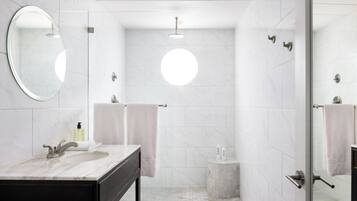 Un baño moderno con un espejo ovalado grande, un lavabo con encimera oscura y una zona de ducha con mampara de cristal.