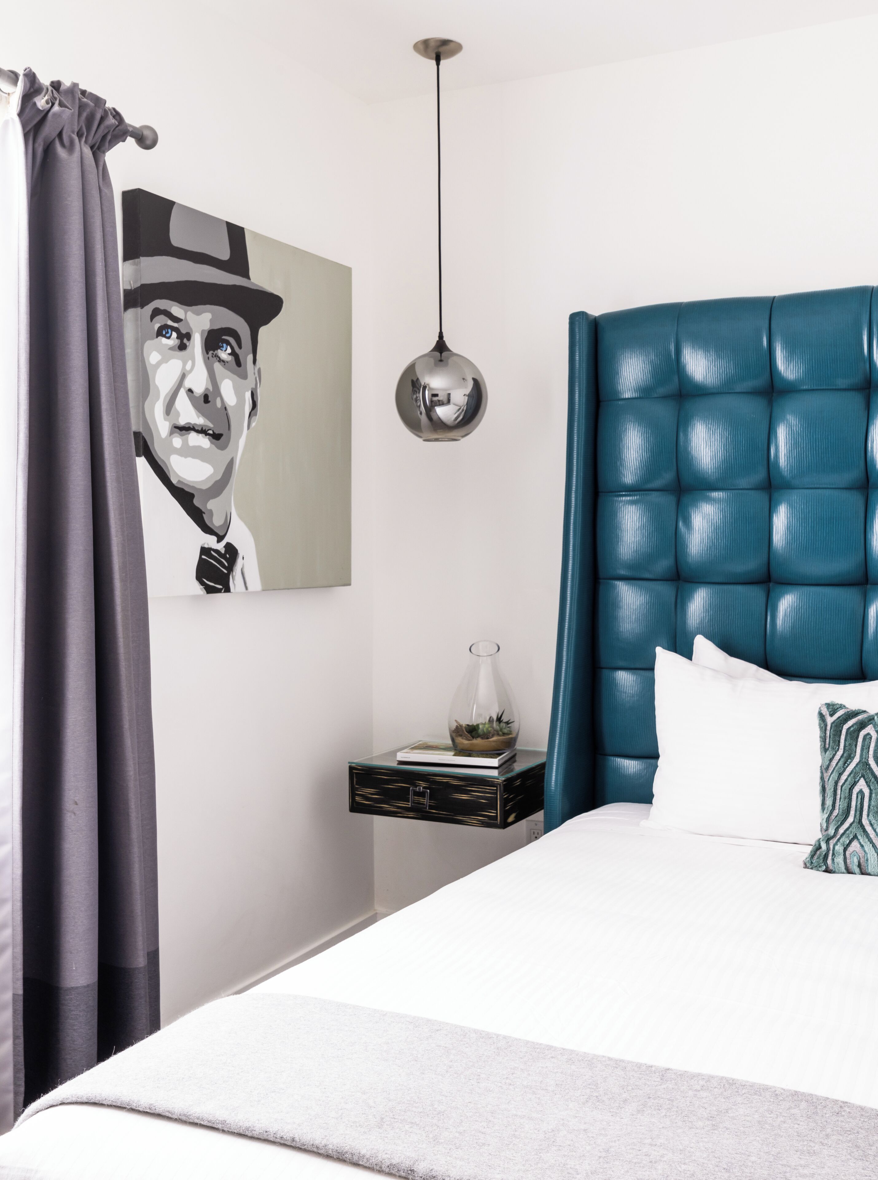 A bedroom with a tufted headboard, a bedside table with a glass vase, and a large framed artwork on the wall.