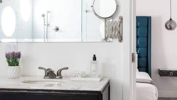 Un baño moderno con tocador blanco, un espejo grande y zona de ducha.