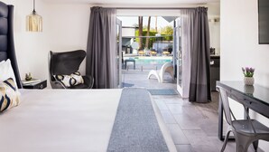 A modern hotel room with a large bed, a desk, a chair, and a view of an outdoor pool area.