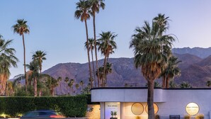 A modern building with palm trees and mountains in the background.