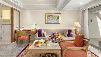 A modern living room with a dining area, a chandelier, a painting on the wall, and a view of the outdoors.