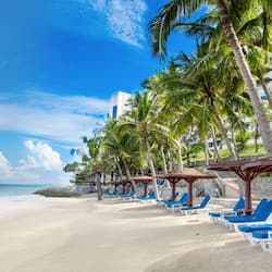 Relax on the beach with sun loungers under shaded umbrellas, overlooking the ocean from a balcony with a stone wall separating the beach from the hotel.