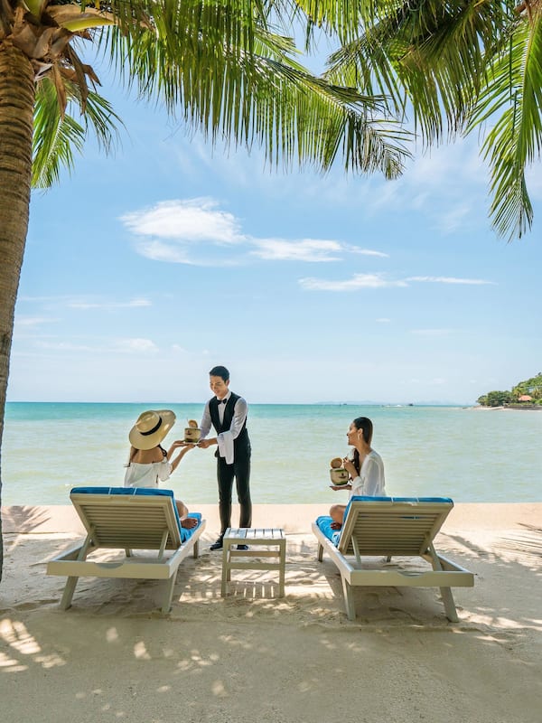 Relax in style with comfortable lounge chairs under the shade of palm trees, served by attentive staff.