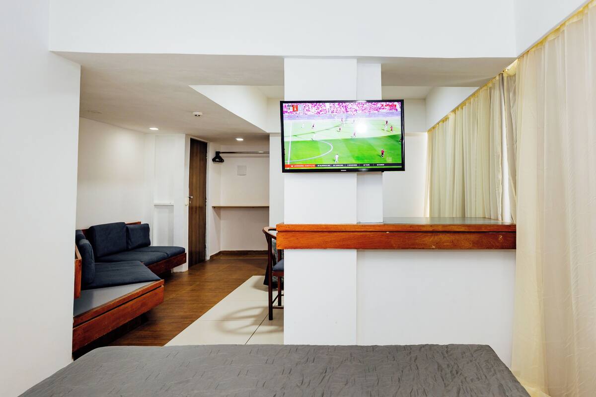Uma sala de estar moderna com uma televisão de tela plana na parede, um banco de madeira, um sofá escuro e uma pequena mesa.