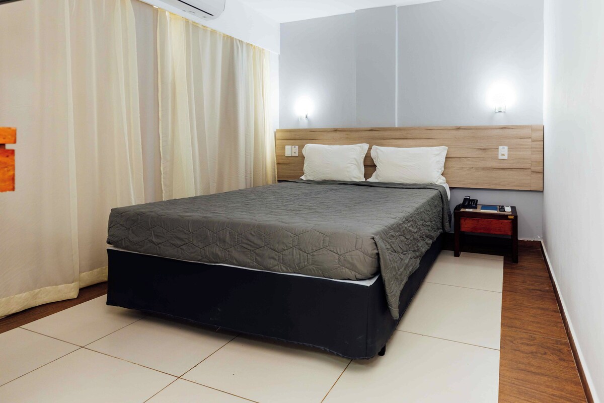 A hotel room with a bed, a nightstand, and a wall-mounted light.