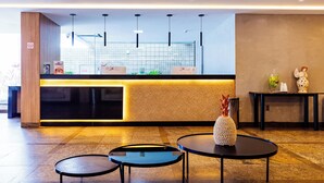 A modern reception area with a counter, two round tables, and a decorative vase. - EL ARAM BEACH BOA VIAGEM (Recife)