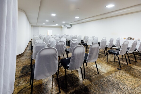 Un salón de conferencias con filas de sillas, una pizarra y una pantalla de proyector.