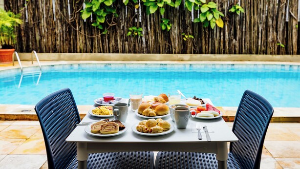 A dining table with breakfast items by a poolside, surrounded by chairs. - EL ARAM BEACH BOA VIAGEM (Recife)