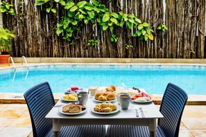 A dining table with breakfast items by a poolside, surrounded by chairs. - EL ARAM BEACH BOA VIAGEM (Recife)