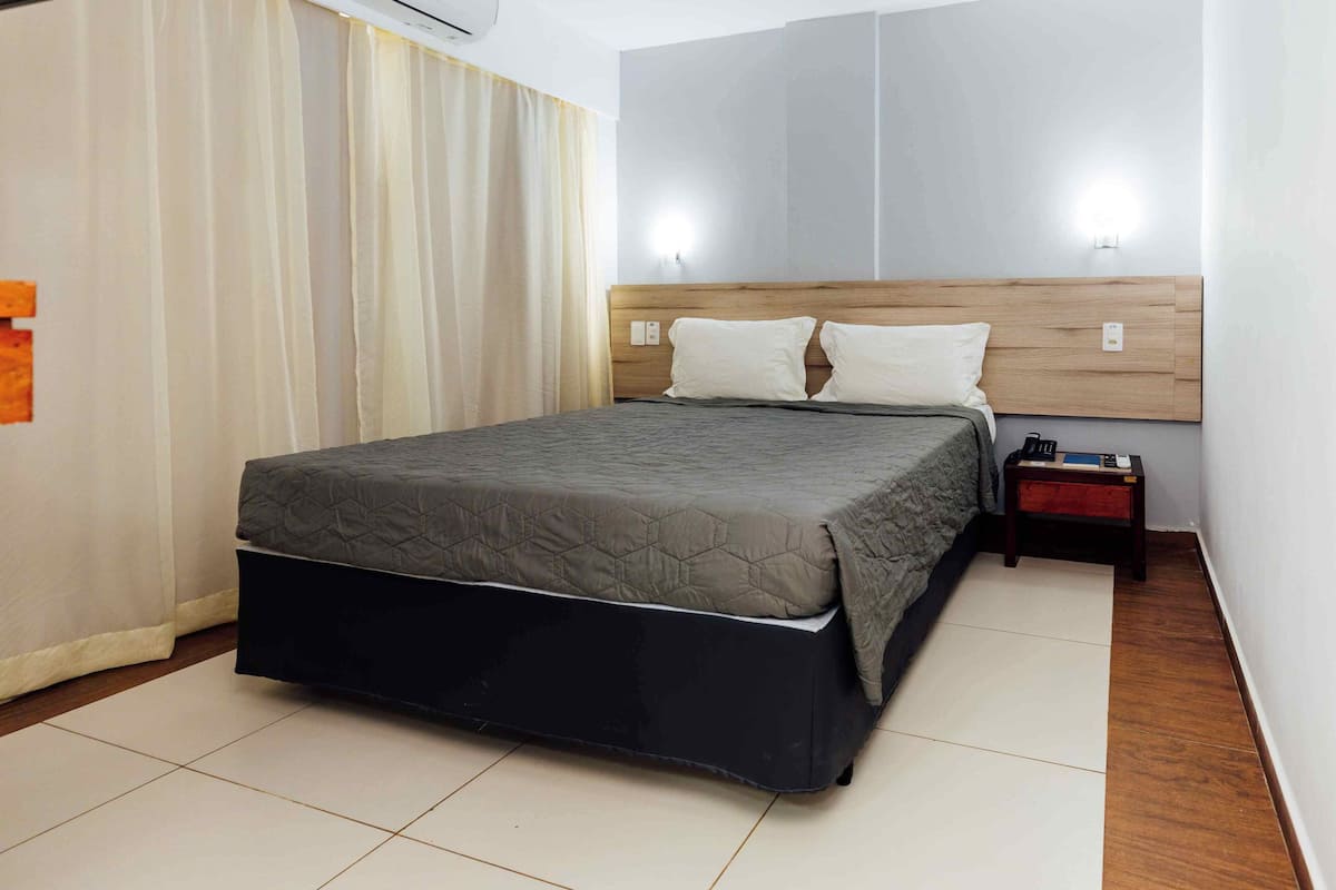 Una habitación de hotel con una cama, una mesita de noche y una lámpara fijada a la pared.