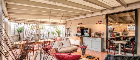 Amplia sala de estar con sofá, sillas y una mesa de comedor. Hay una zona de cocina con armarios y un refrigerador. La habitación tiene ventanas grandes y un techo con vigas a la vista.