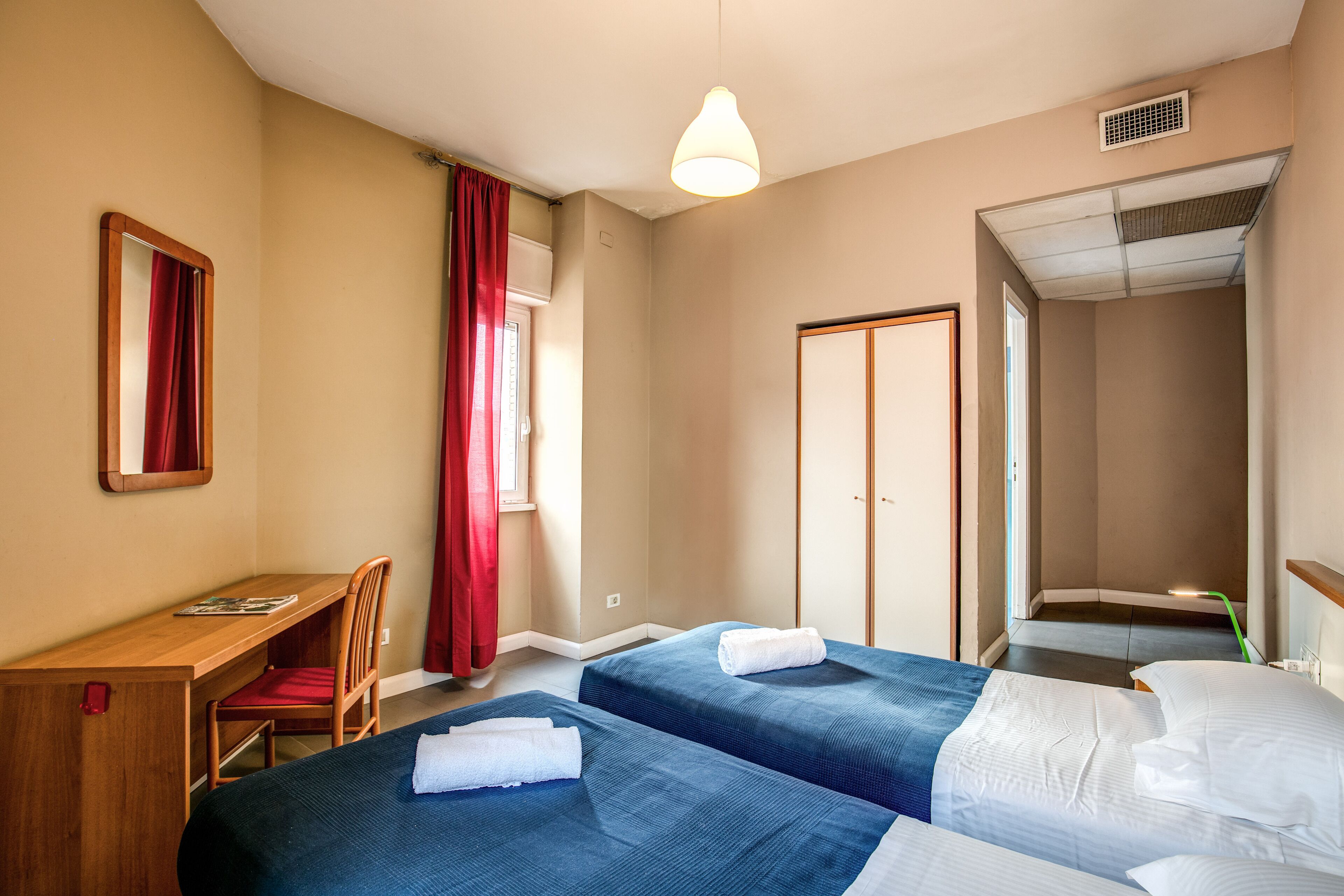 A hotel room with two beds, a desk, and a chair.