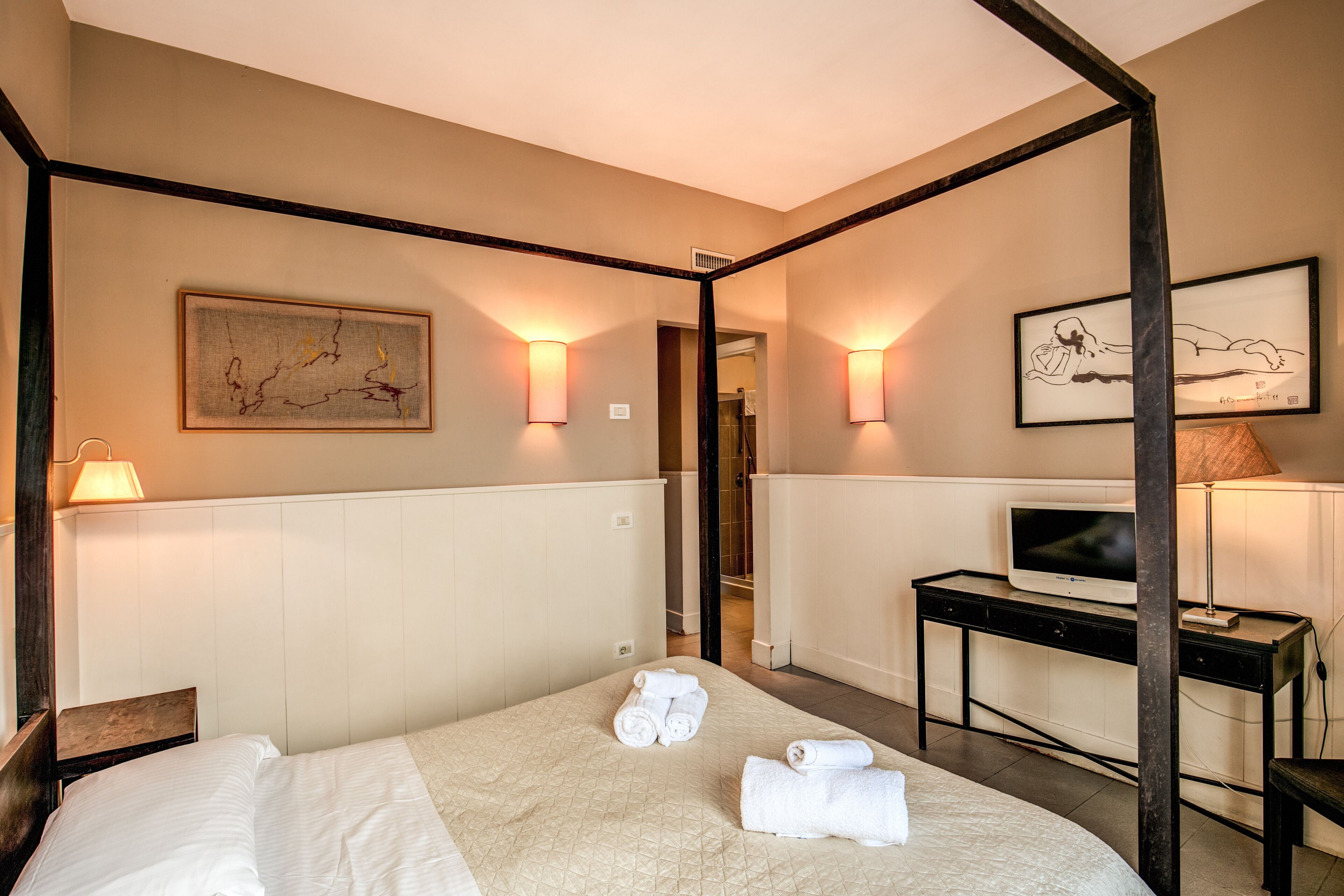 A hotel room with a bed, a desk with a TV, and artwork on the walls.