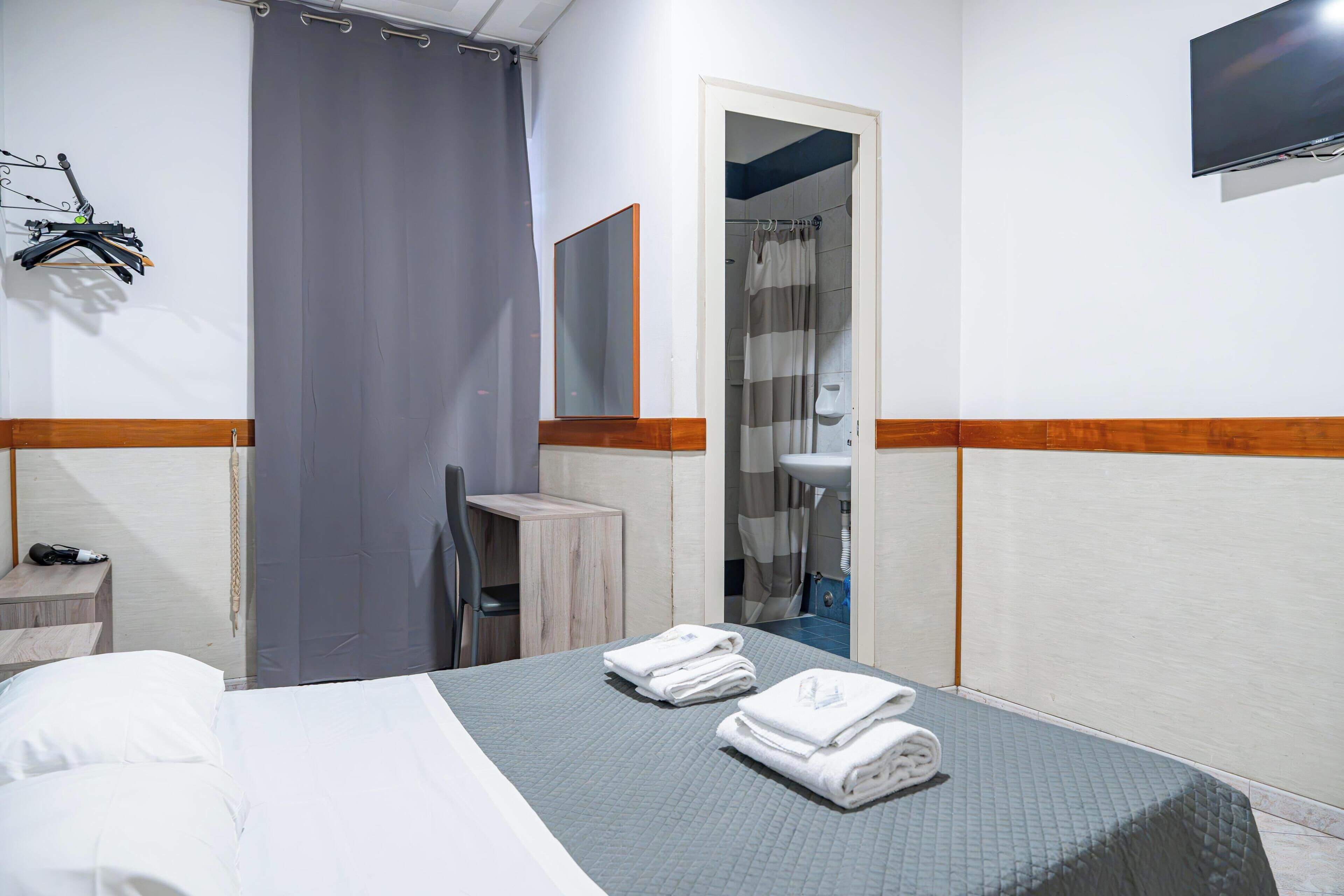 Une chambre d’hôtel comprenant un lit, un bureau, une chaise, une salle de bain avec douche et un téléviseur fixé au mur.