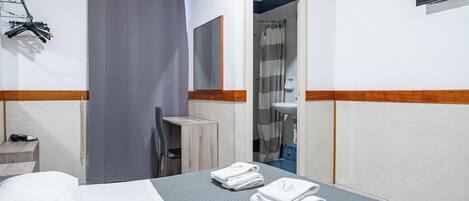 Une chambre d’hôtel comprenant un lit, un bureau, une chaise, une salle de bain avec douche et un téléviseur fixé au mur.