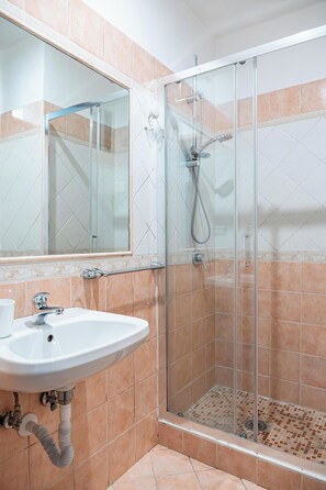Un baño con ducha de mampara de vidrio, un lavabo con espejo y paredes de azulejos.