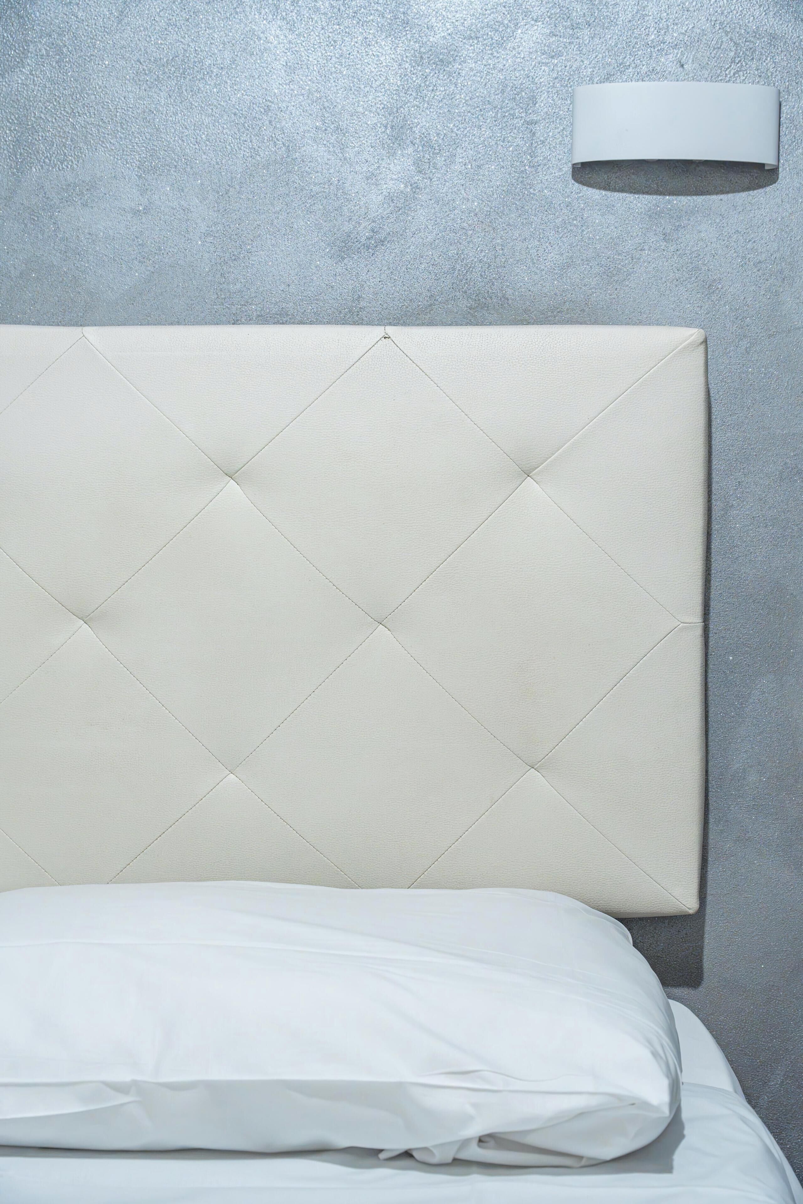 A bed with a quilted headboard against a textured wall.