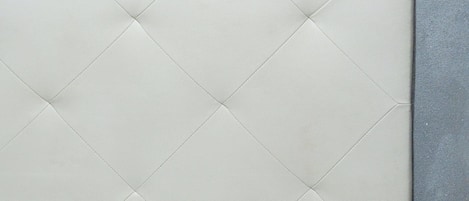 A bed with a quilted headboard against a textured wall.