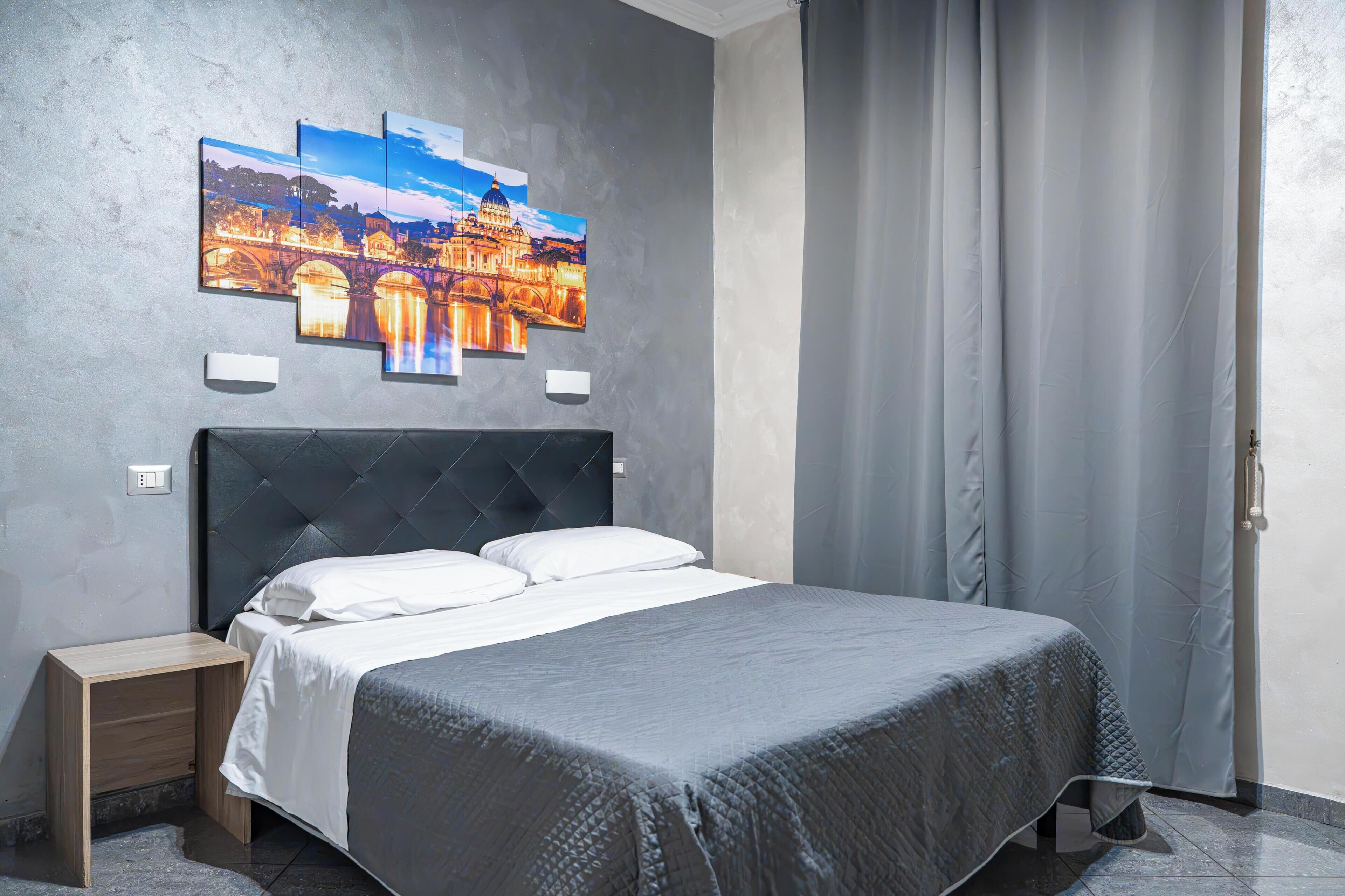 Un dormitorio moderno con una cama grande, una mesita de noche, una lámpara de pared y un cuadro de un paisaje urbano.