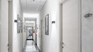 A long, narrow hotel corridor with doors on both sides, numbered room signs, and framed pictures on the walls. - Hotel Planet (Rome)
