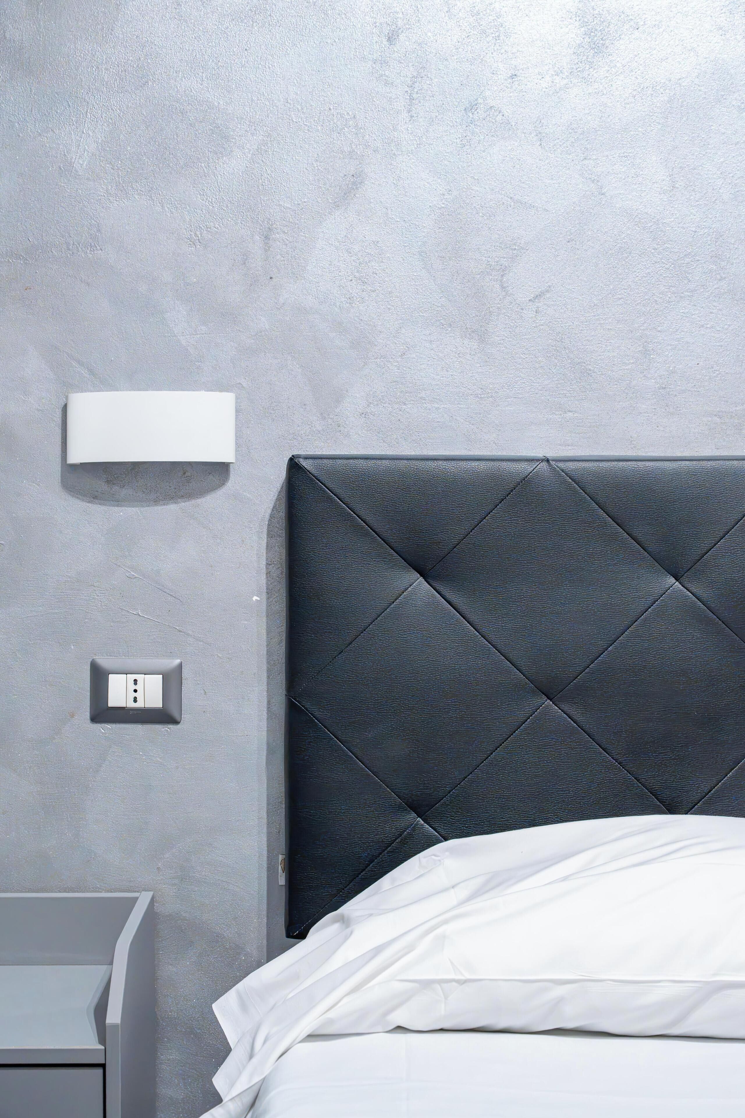 A modern bedroom with a quilted headboard, a bedside table, and a wall-mounted light fixture.