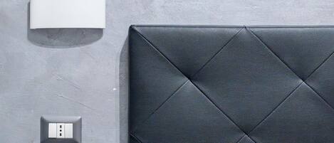 A modern bedroom with a quilted headboard, a bedside table, and a wall-mounted light fixture.
