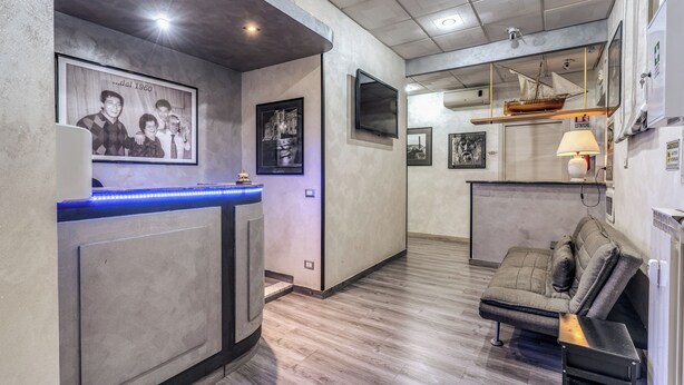 A reception area with a counter, framed photos, and a seating area with a couch and a small table. - Hotel Planet (Rome)