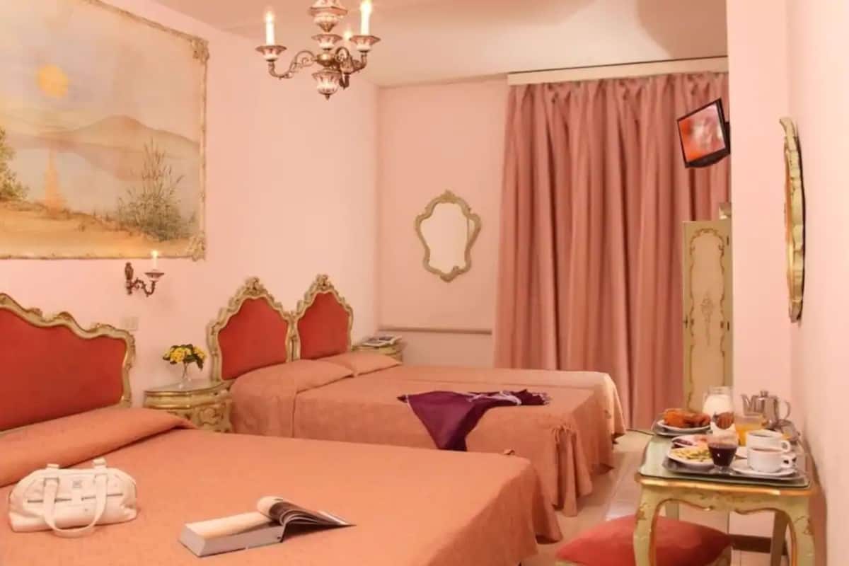 Habitación de hotel con dos camas, un candelabro, un cuadro, un espejo y una bandeja de desayuno.