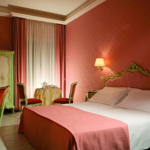 A hotel room with a bed, two chairs, a table with a lamp, and a window with curtains.