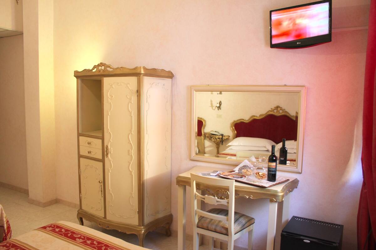 Habitación de hotel con un armario grande, una mesita de noche con espejo y un televisor montado en la pared.