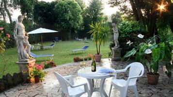 A patio area with a statue, a table with chairs, and a lawn with lounge chairs.