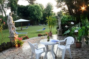 A patio area with a statue, a table with chairs, and a lawn with lounge chairs.