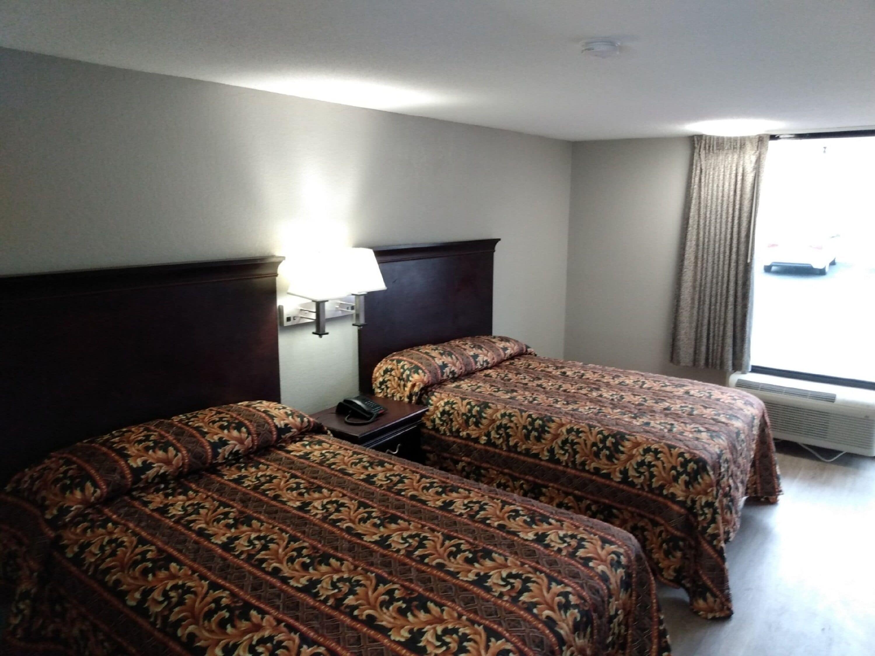 A hotel room with two beds, a nightstand, a lamp, and a window with curtains.