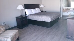 A bedroom with a large bed, two bedside tables with lamps, a small chair, and a mirror above the sink. - Gateway Inn - Savannah (Savannah)