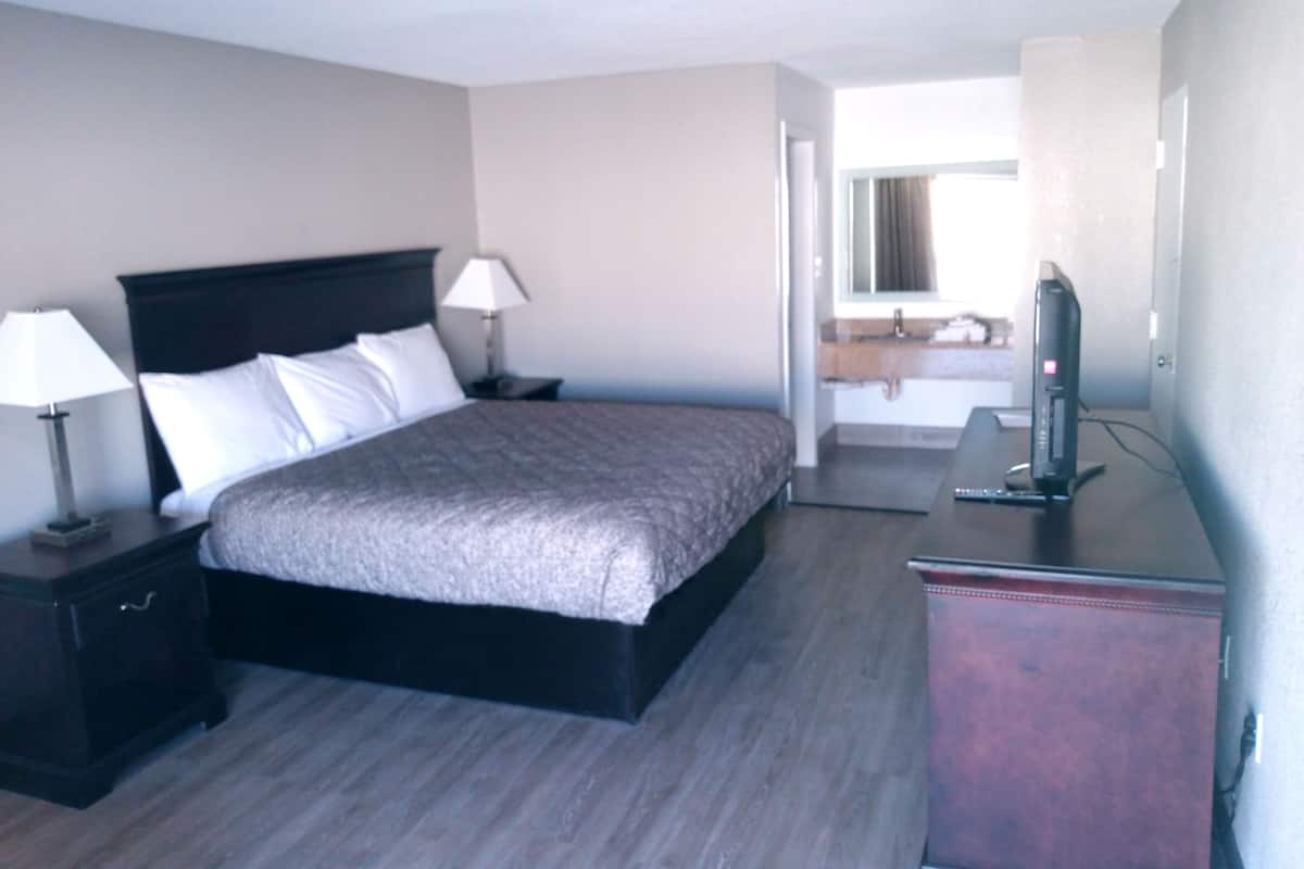 Une chambre d’hôtel avec un grand lit, une table de chevet avec une lampe, une commode et un téléviseur.