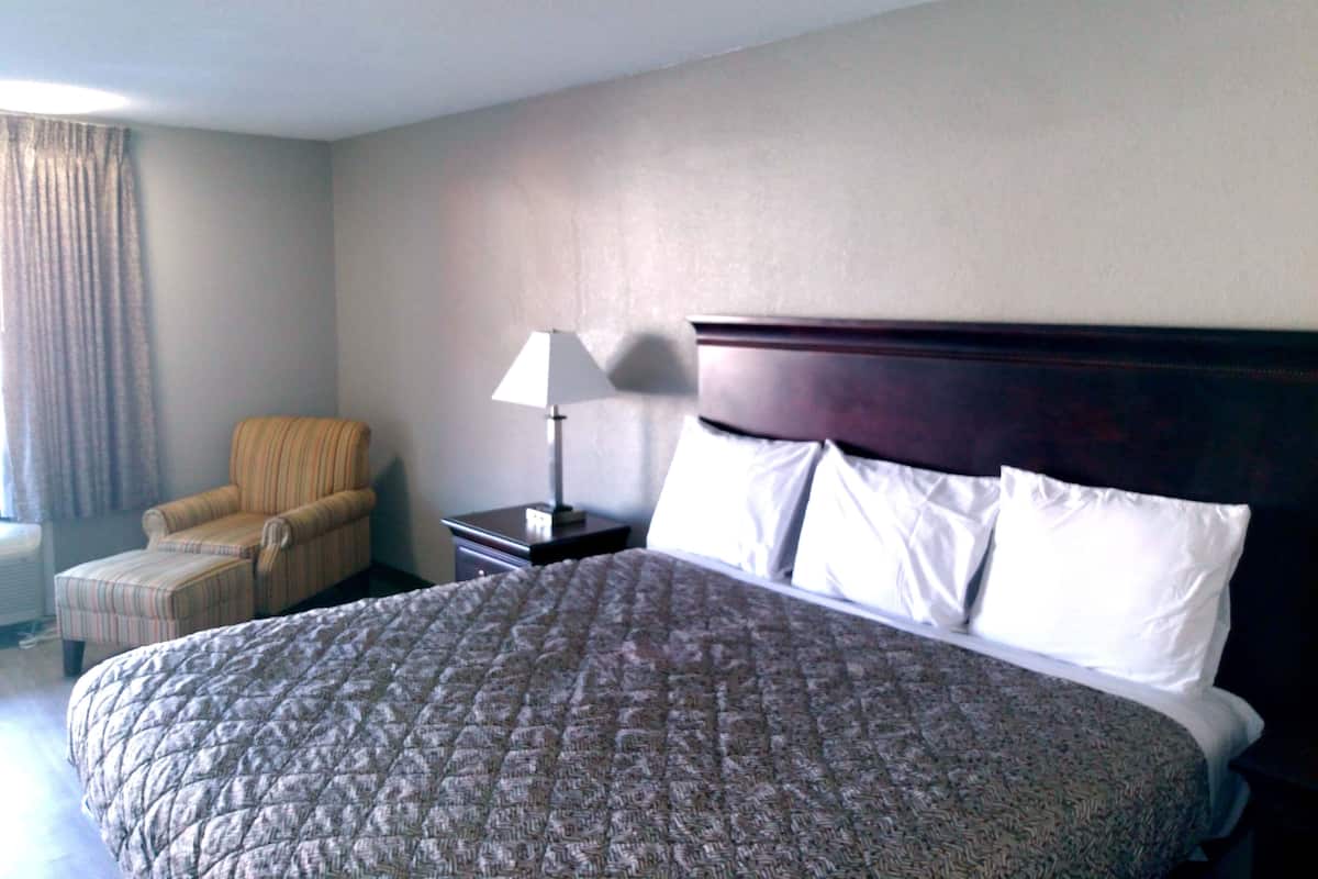 Une chambre d’hôtel avec un grand lit, une chaise, une table de chevet et une lampe.