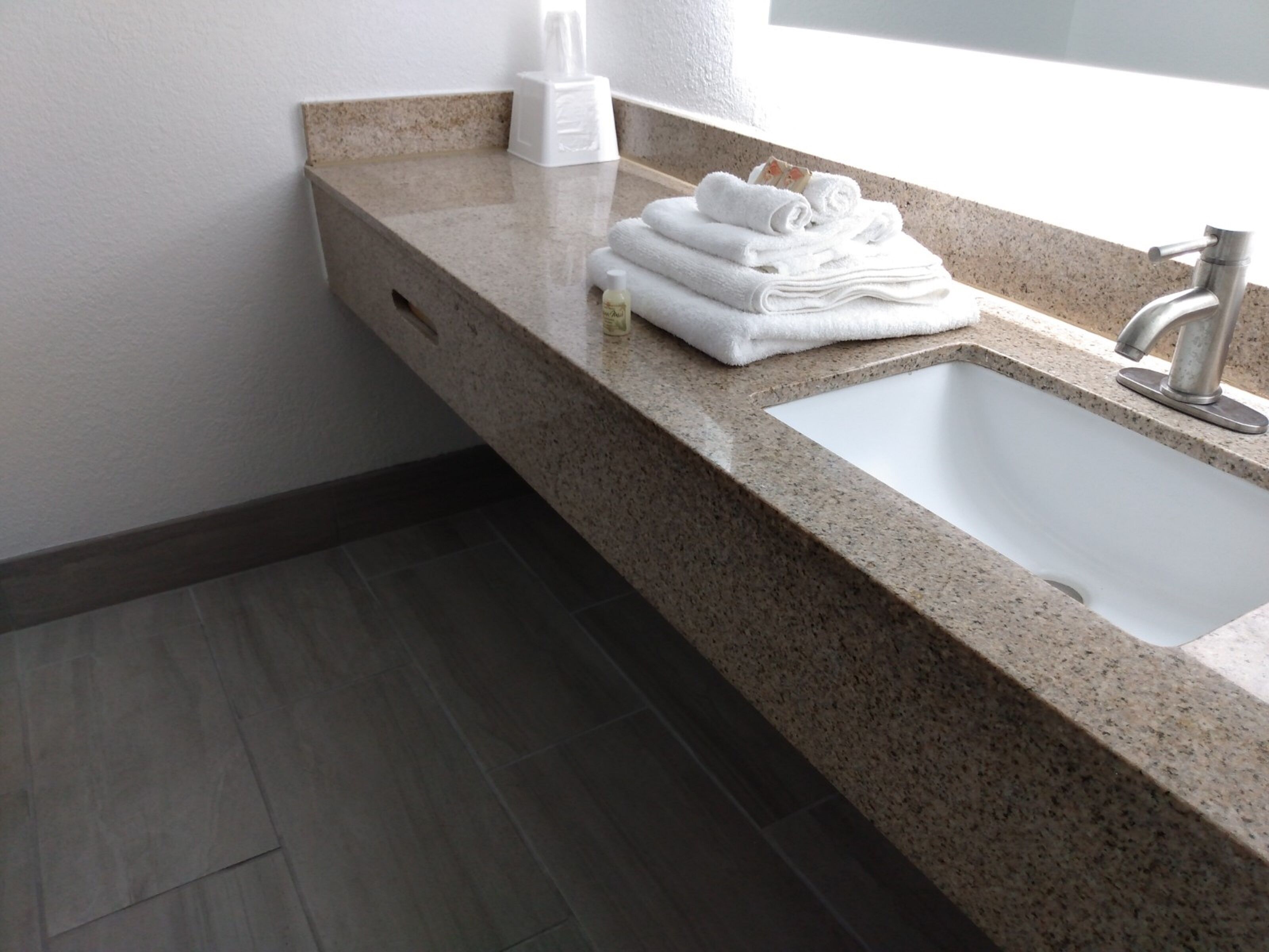 Une salle de bain avec un comptoir en granit, un lavabo blanc et un distributeur de serviettes.