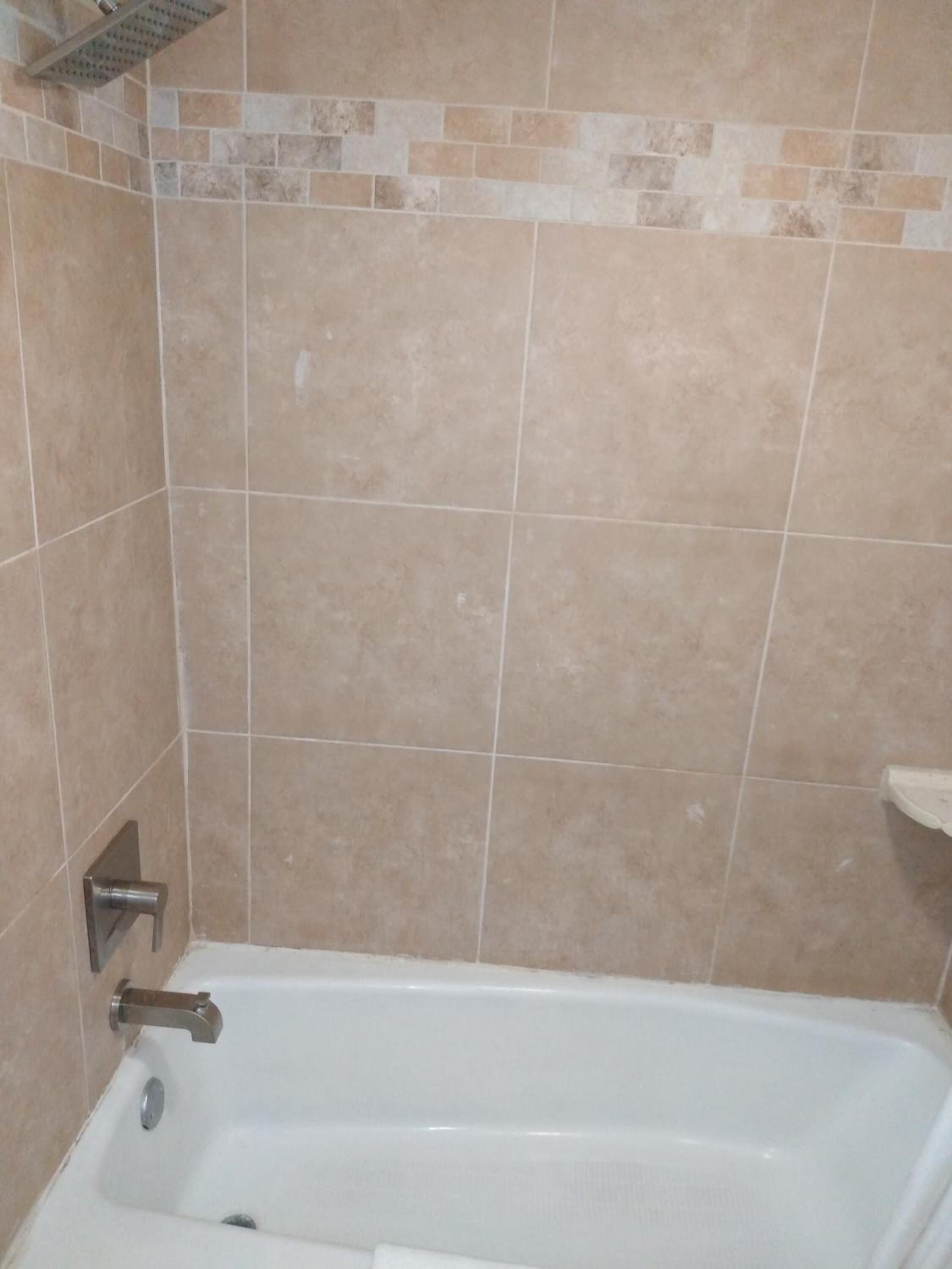 A bathroom with beige tiles, a white bathtub, and a showerhead.