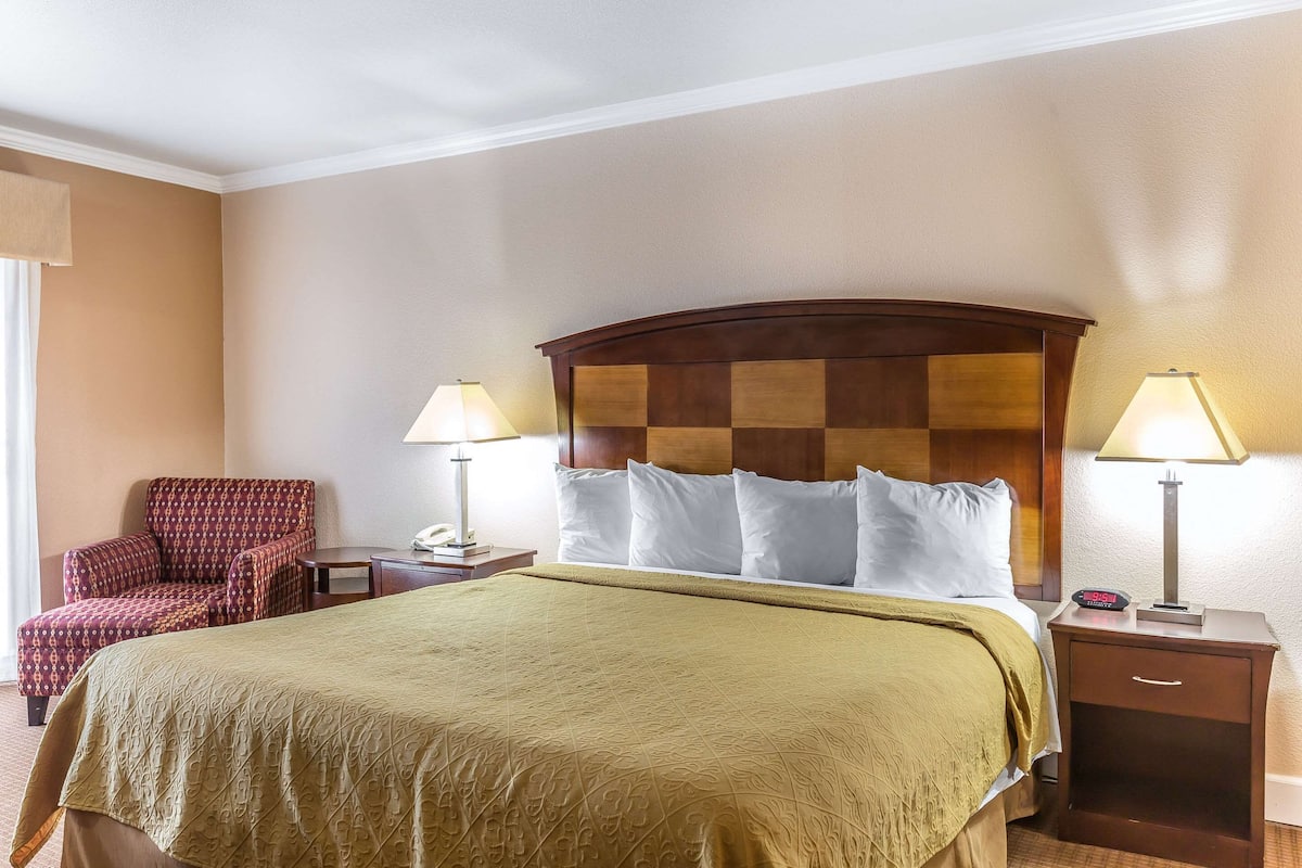 A hotel room with a large bed, two bedside tables, a chair, and a lamp.