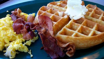 A plate with scrambled eggs, bacon, and a waffle with butter.